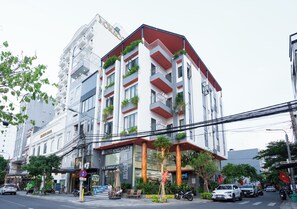 A multi-story hotel with balconies, a convenience store, and a visible sign for a nearby market. - Viet Apartments (Da Nang)