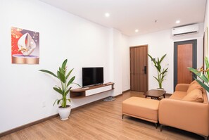 A modern living room with a flat-screen TV on a wooden stand, a sofa, and two potted plants. - Viet Apartments (Da Nang)