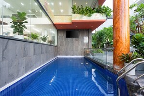 A swimming pool with a blue tiled floor, surrounded by glass walls and potted plants. - Viet Apartments (Da Nang)
