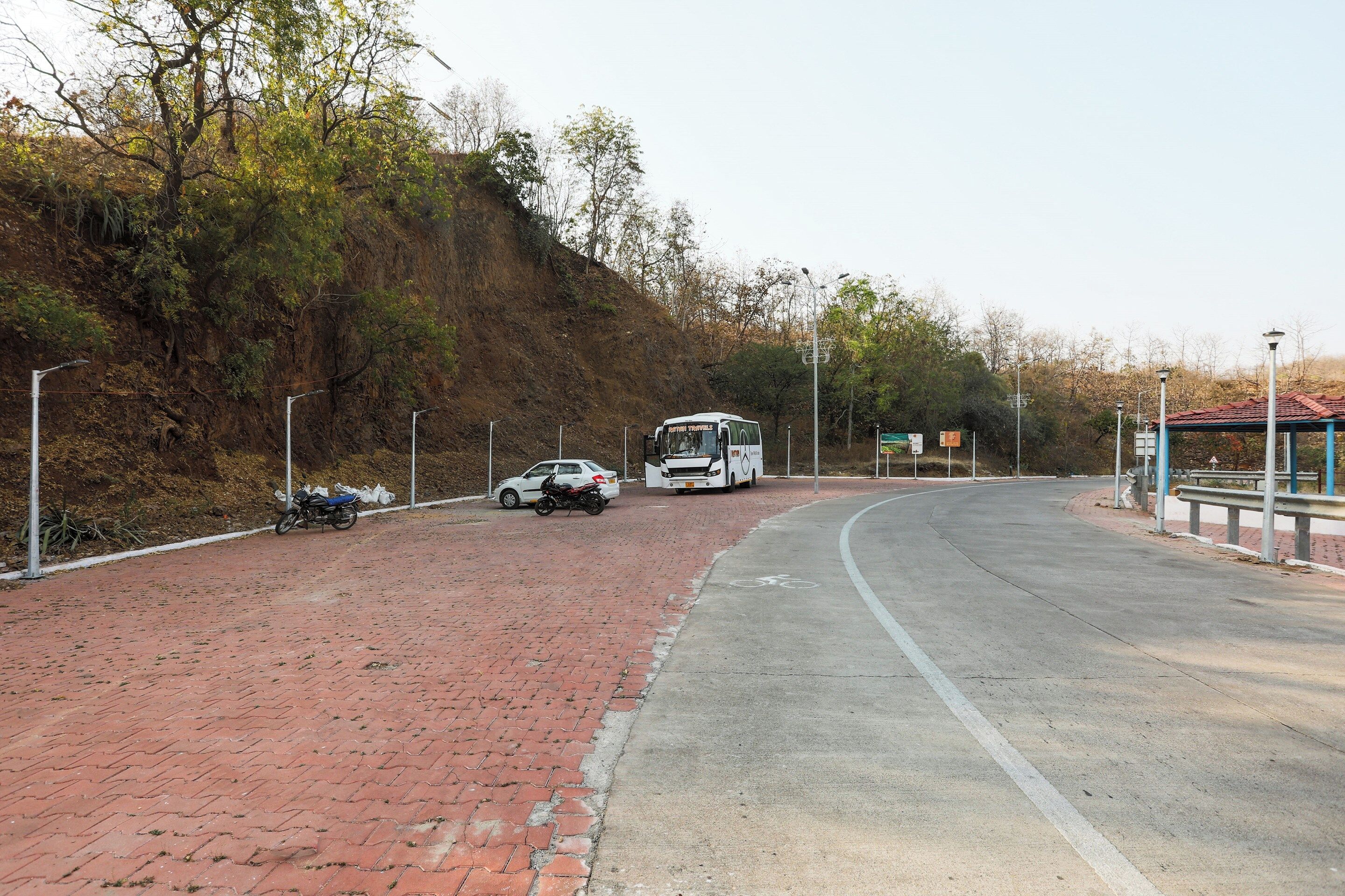 A paved road with a brick sidewalk, a white bus, and a motorcycle parked on the side.