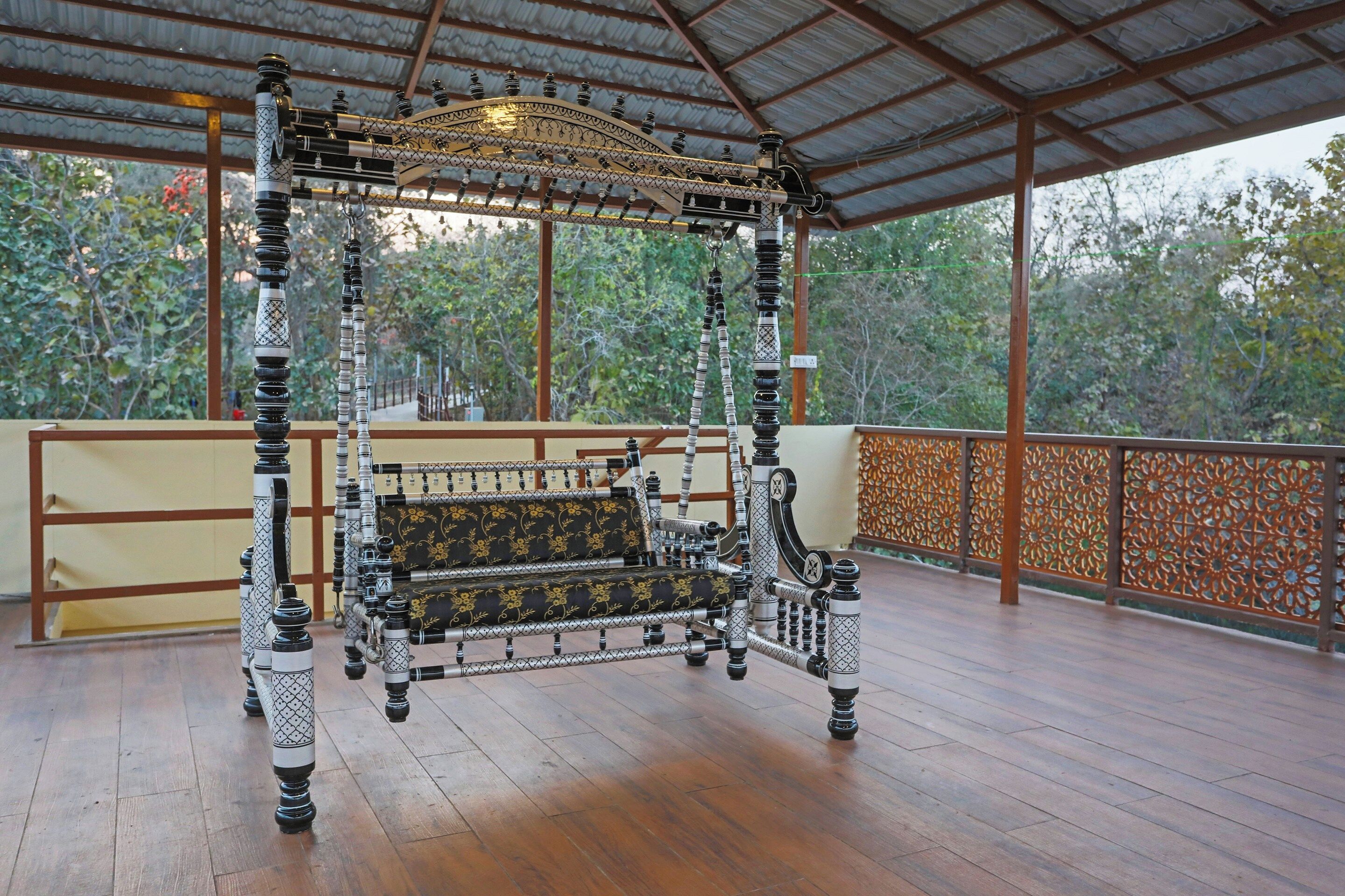 A four-poster bed with intricate black and white patterns, a bench with floral upholstery, and a wooden floor.