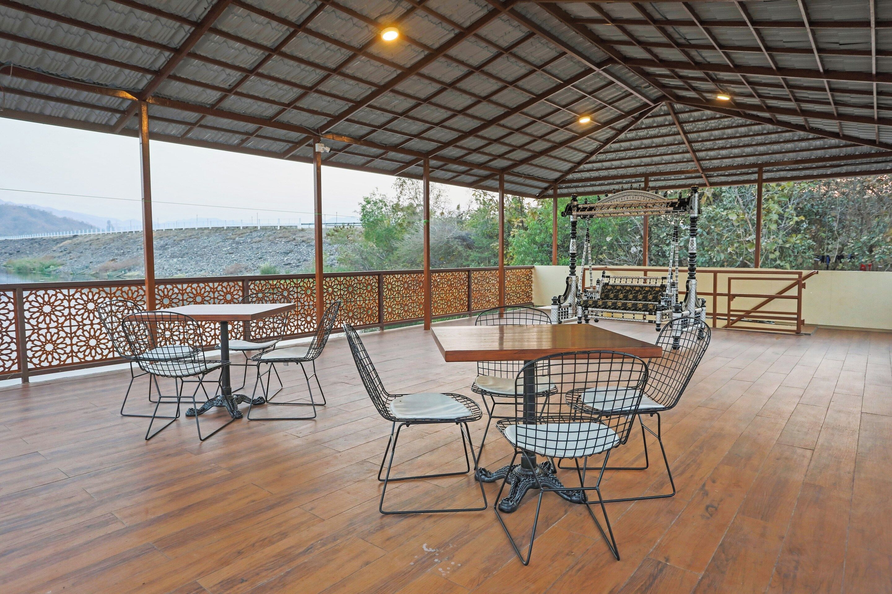 An outdoor patio with a wooden table and chairs, a decorative railing, and a view of the landscape.