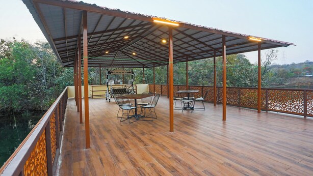 A covered outdoor area with wooden flooring, metal railings, and a table with chairs. - Ekta Houseboat Statue Of Unity Kevadia (Vadodara)
