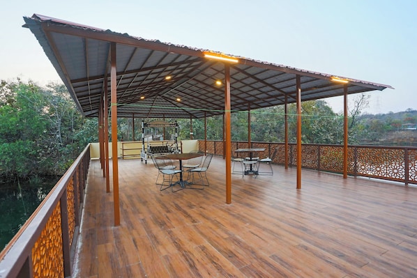 A covered outdoor area with wooden flooring, metal railings, and a table with chairs. - Ekta Houseboat Statue Of Unity Kevadia (Vadodara)