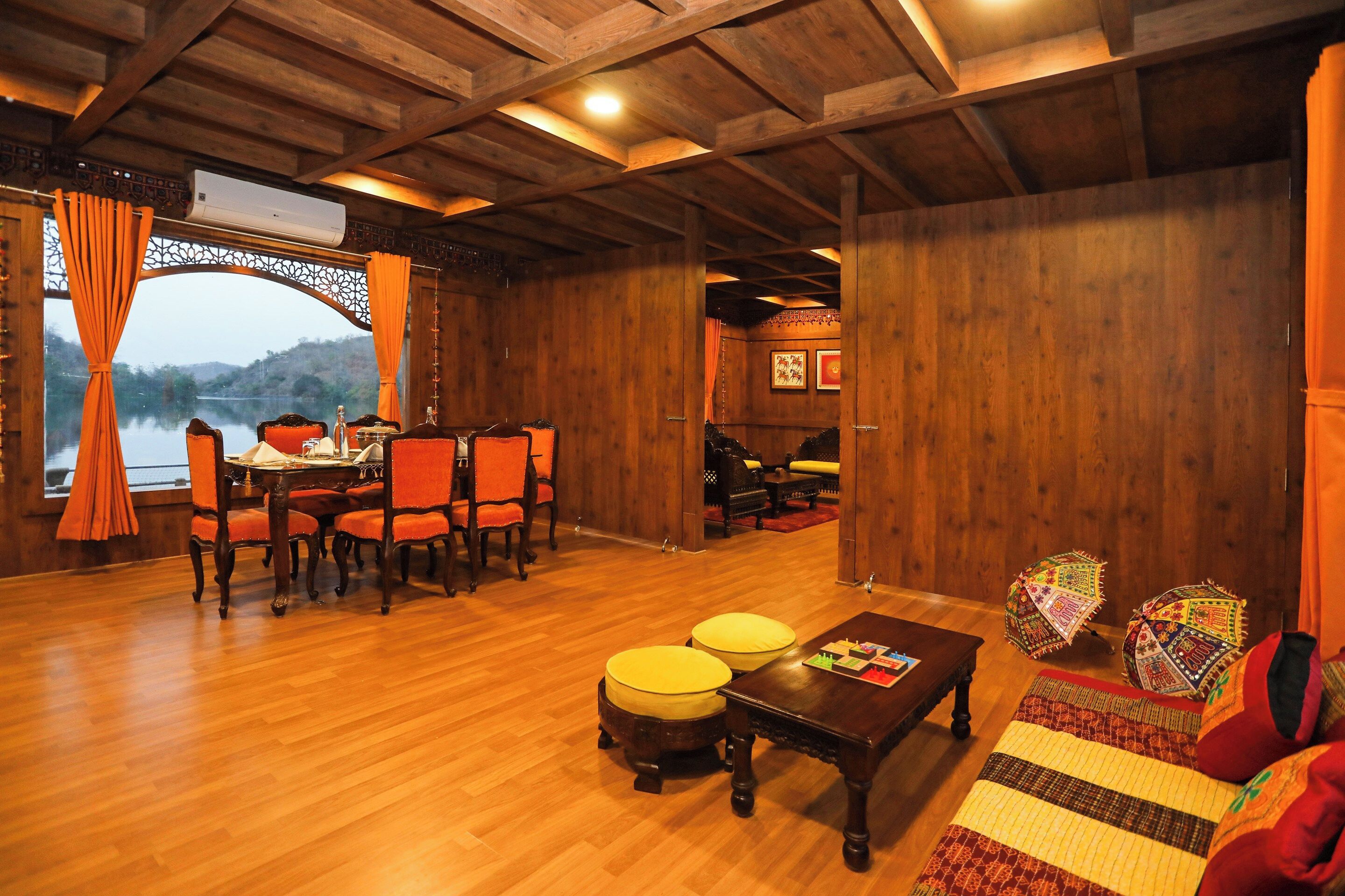 A wooden interior with a dining area, a sofa set, and a view of a lake.