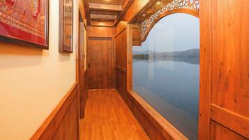 Un estrecho pasillo de madera con una puerta al final, una ventana con vista a una masa de agua y un cuadro en la pared.