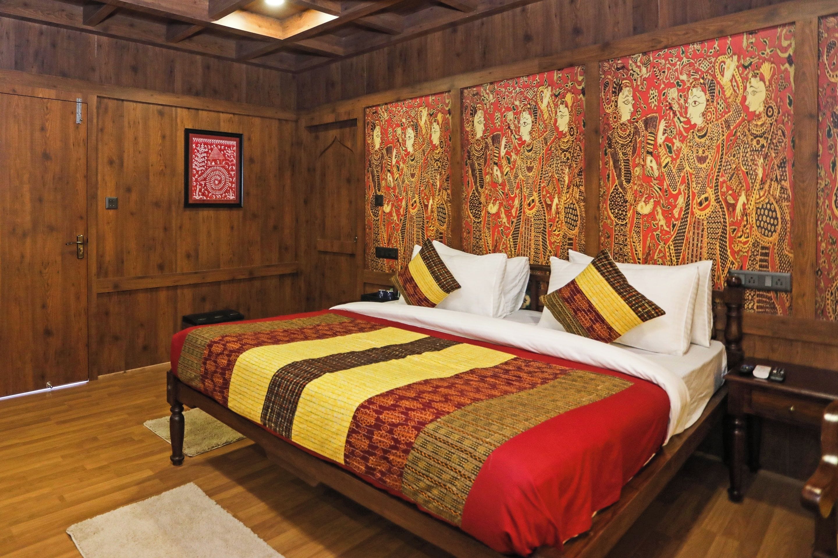 Una habitación con paneles de madera, una cama grande, una colcha de edredón estampada en rojo y amarillo, y un tapiz rojo y dorado en la pared.