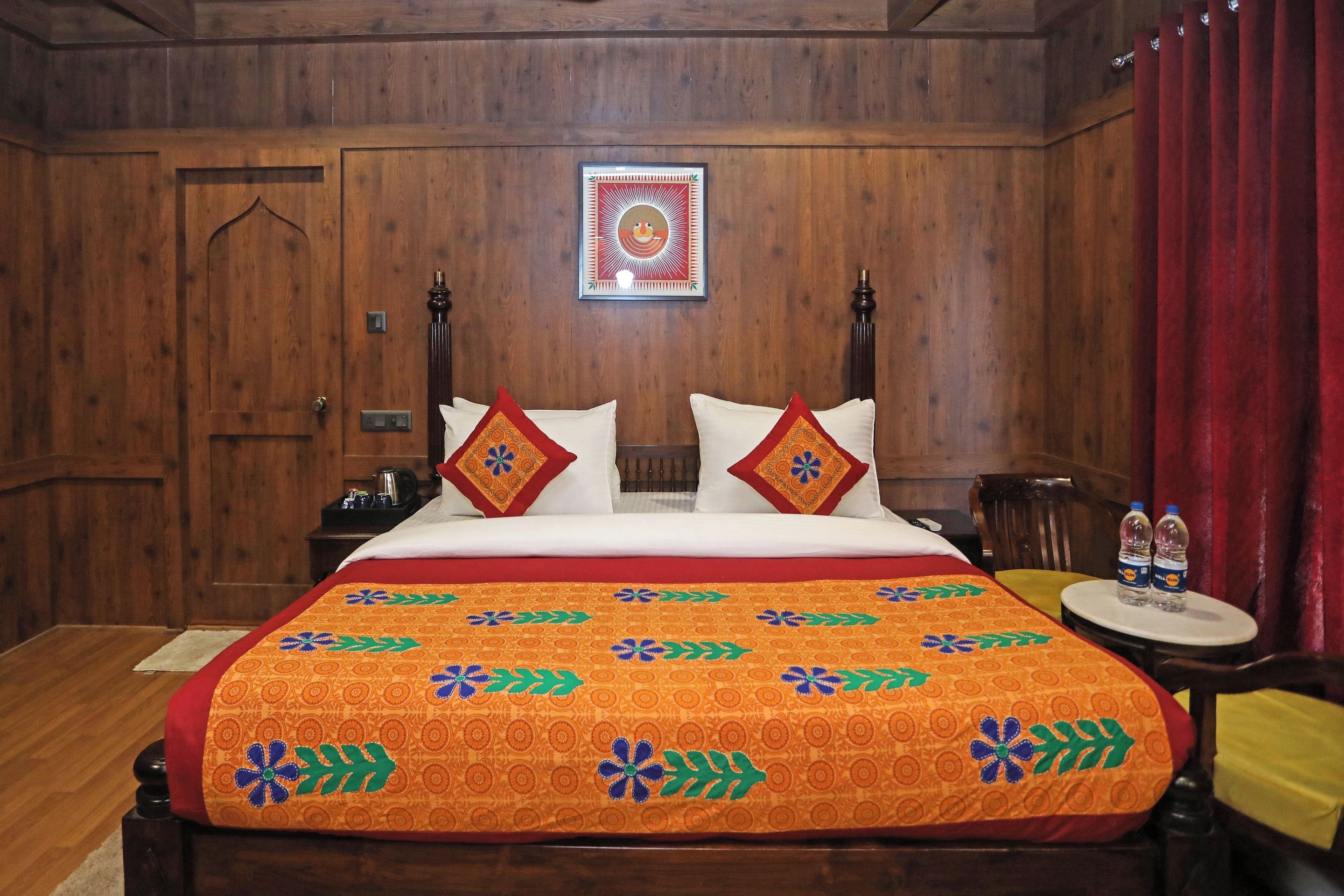 Habitación con paneles de madera, una cama, almohadas, un cuadro enmarcado y una mesita con botellas.