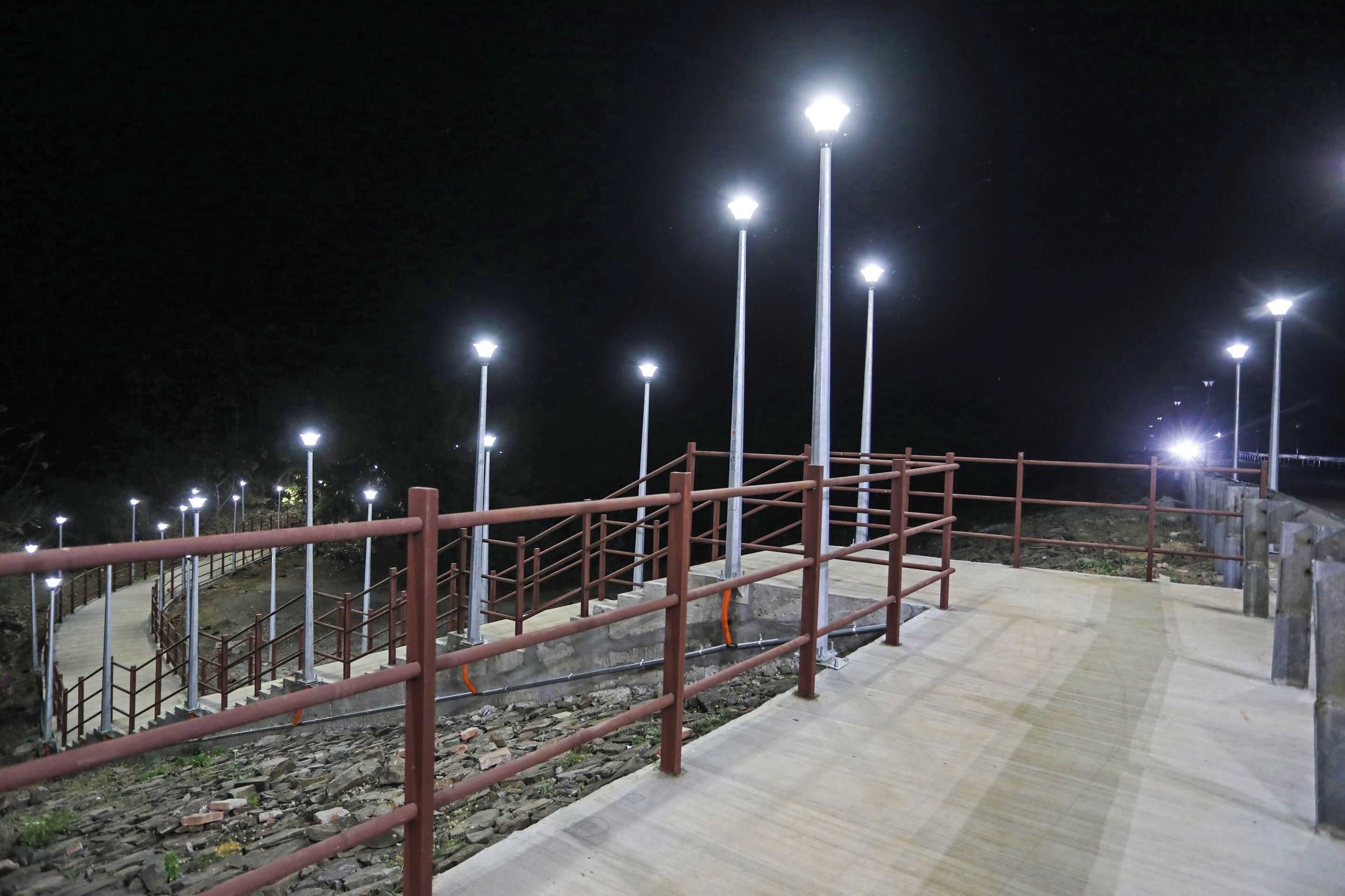 Un espace extérieur aménagé pour la nuit, avec un chemin en béton, des garde-corps en métal et plusieurs lampadaires.