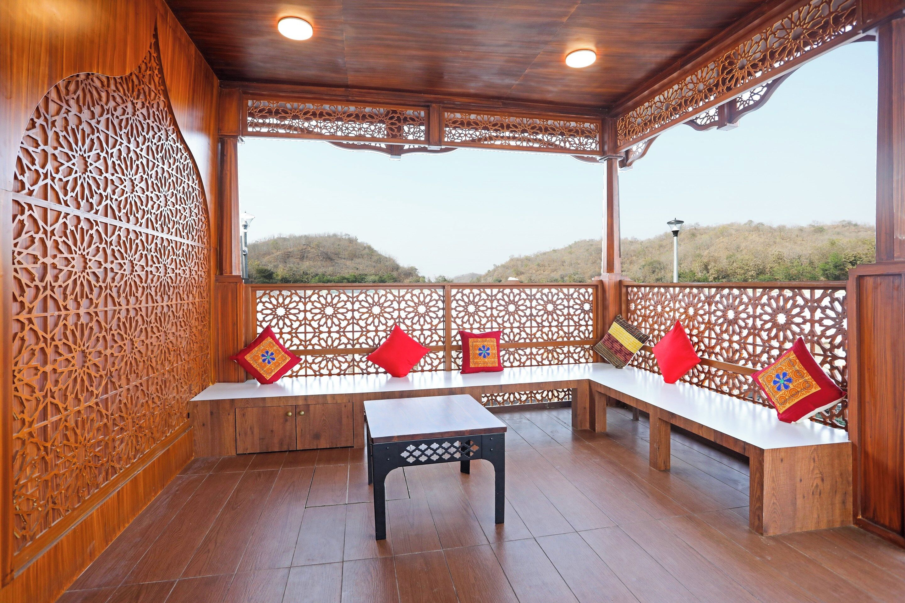 A covered outdoor seating area with wooden benches and a table, surrounded by intricate wooden lattice panels.