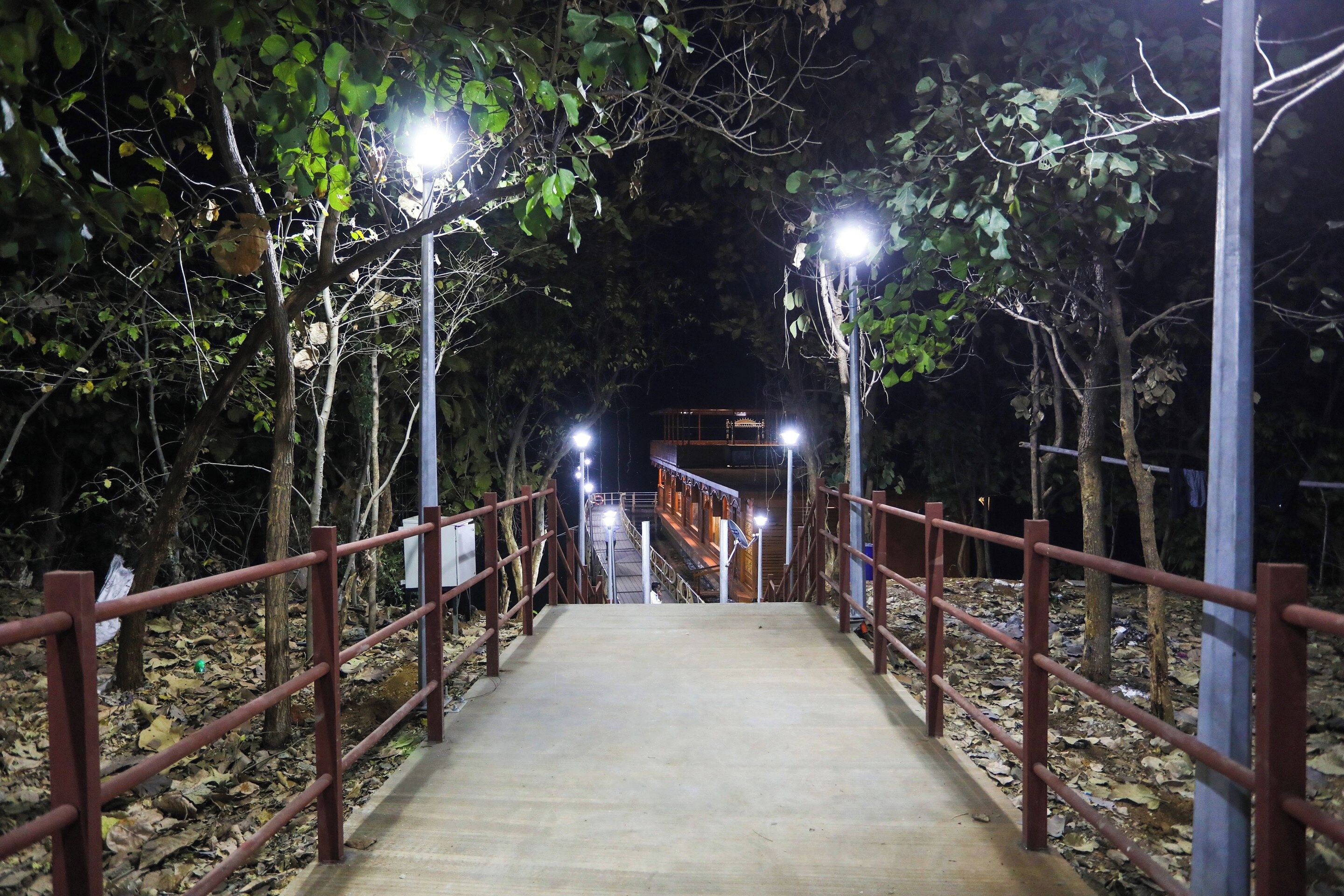 A nighttime walkway with metal railings and overhead lighting, leading to a structure in the distance.