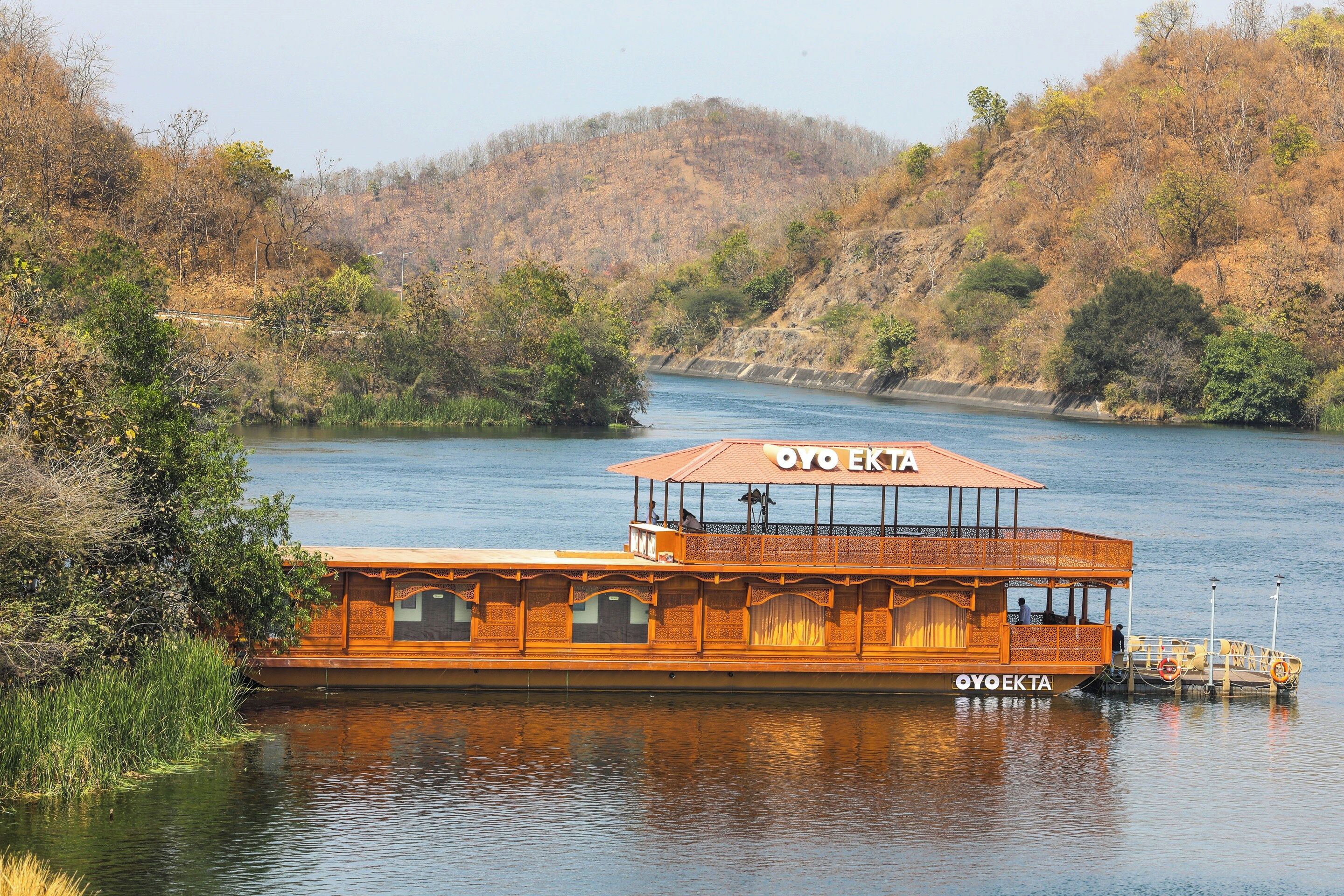 Una embarcación de madera con cubierta superior protegida y un letrero que dice 'OYO EKTA' en el costado.