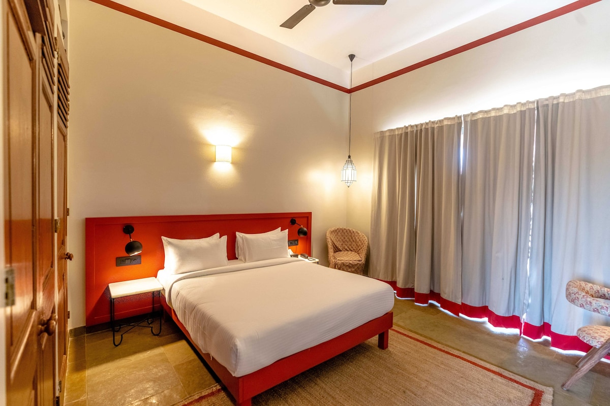 Ein Hotelzimmer mit Bett, Nachttisch, Sessel und einem Fenster mit Vorhängen.