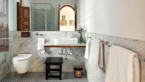 Ein Badezimmer mit Marmorboden, einem weißen Waschbecken, einer Toilette, einem kleinen Holzschemel und einem Spiegel über dem Waschbecken.