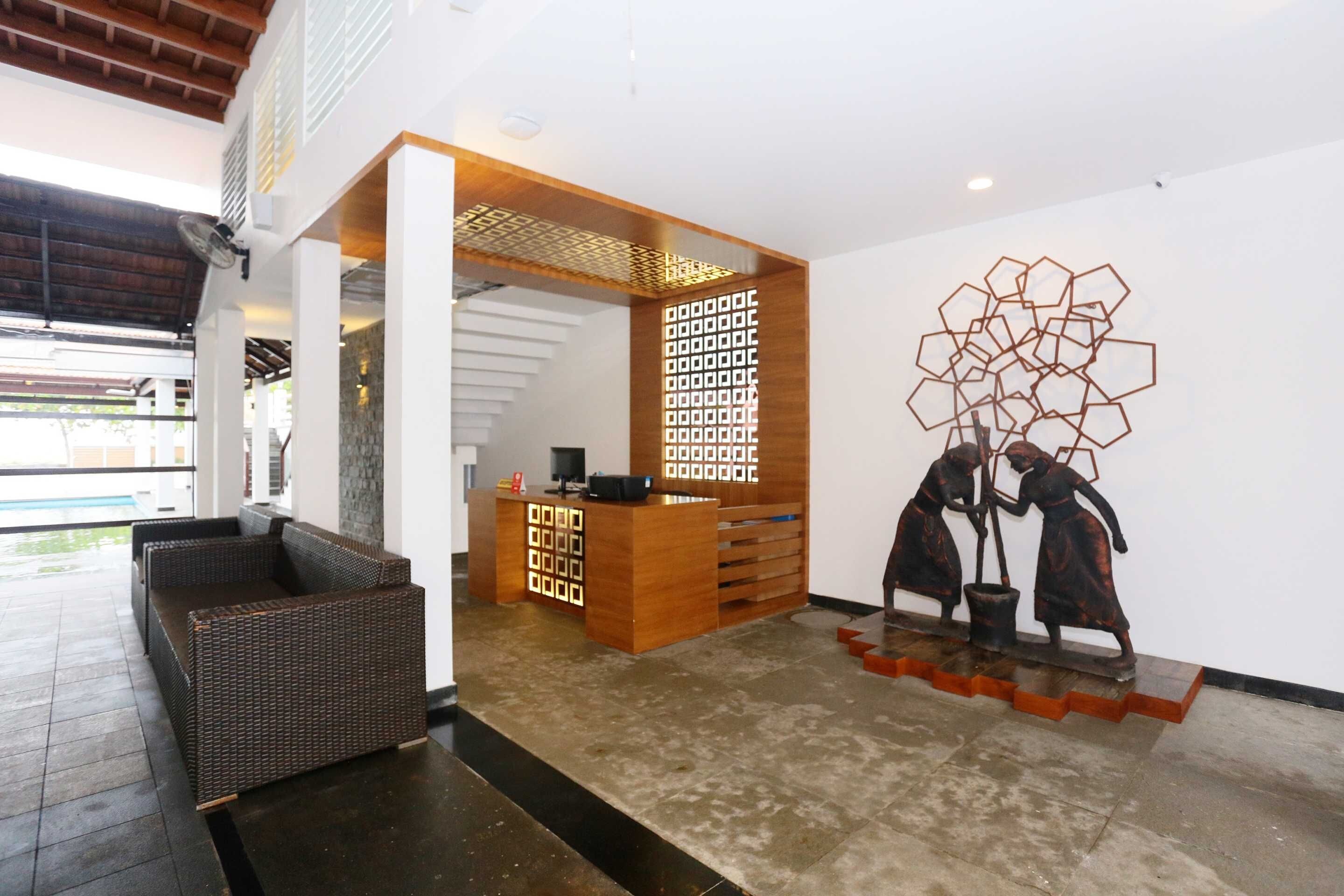 Una zona de recepción con un escritorio de madera, un área de estar con mobiliario de mimbre y una pared con una escultura geométrica.