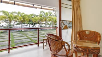A balcony with wicker furniture, a glass table, and a view of a landscaped area with palm trees.