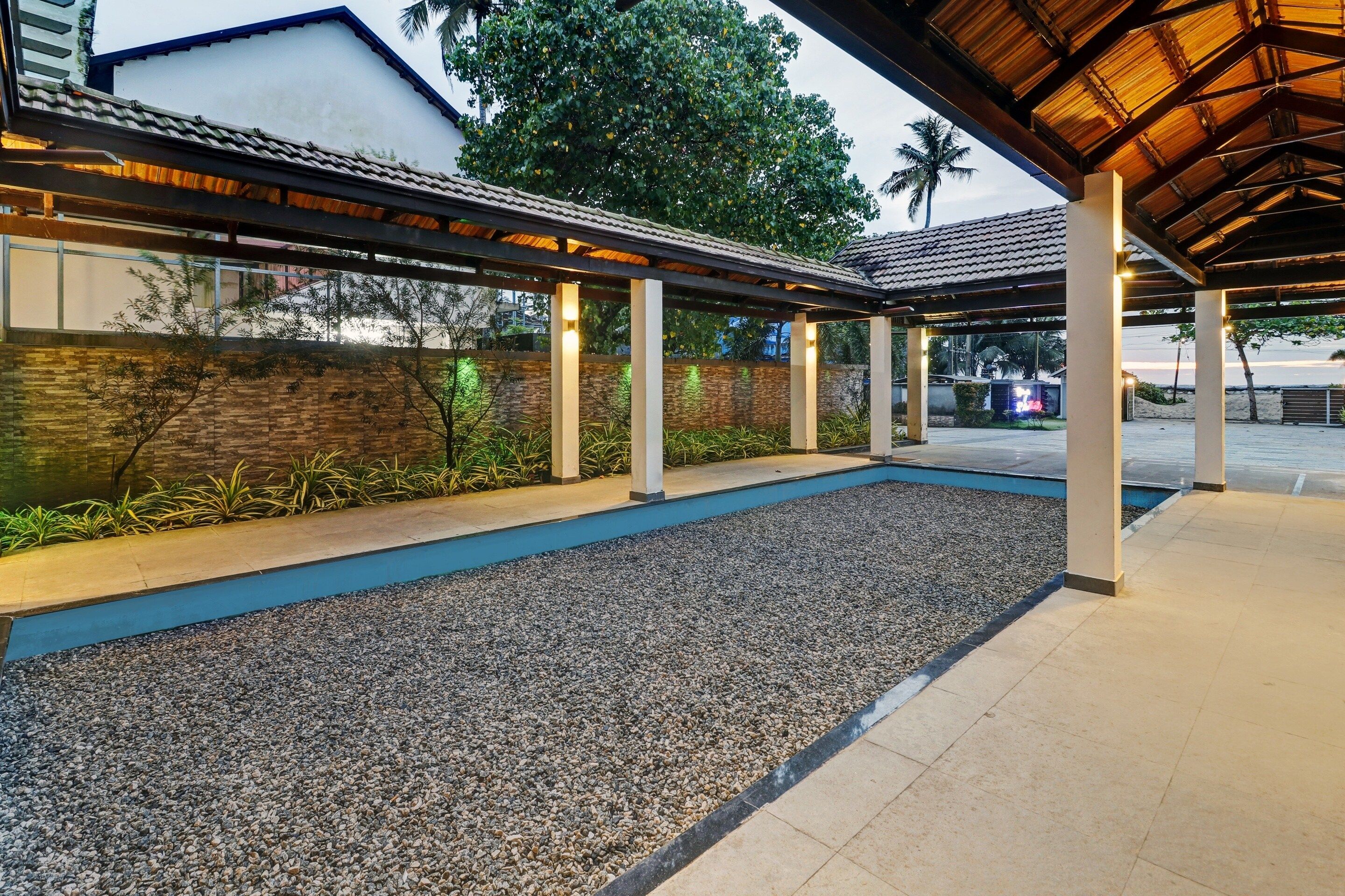 An outdoor covered area with a pool, surrounded by plants and a stone wall.