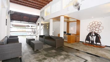 Un amplio vestíbulo con vista a la piscina, muebles de mimbre y un mostrador de recepción.