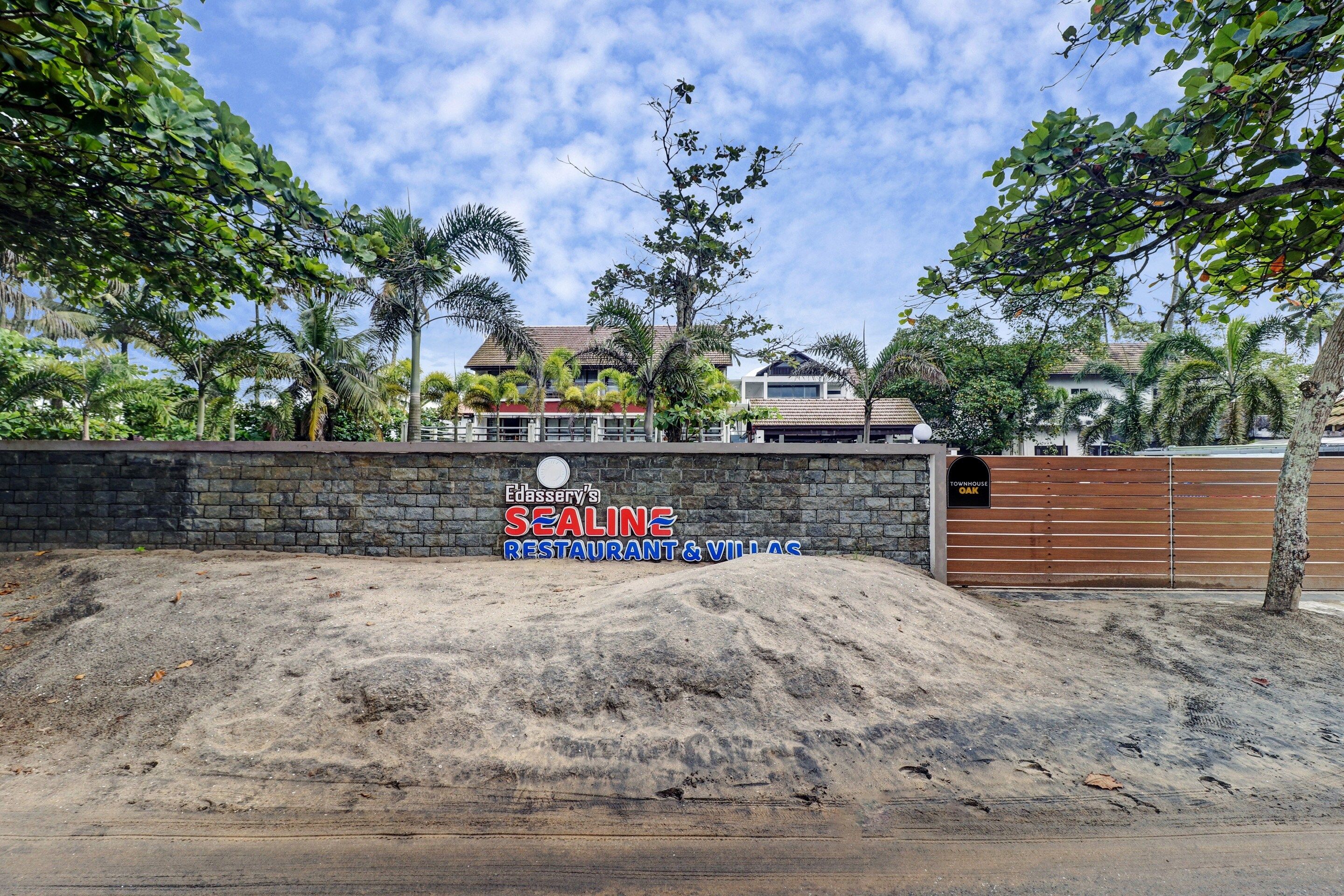 A sign for Edassery's Sealine Restaurant & Villas with a stone wall and a wooden gate.