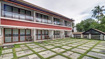 Un edificio de dos pisos con un balcón, un área de estar techada al aire libre y un patio empedrado con borde de césped.