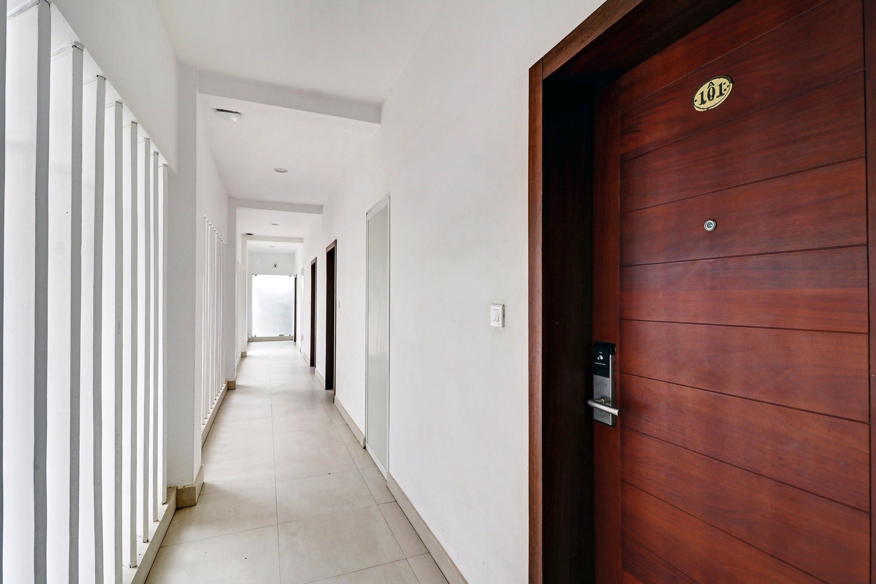 A corridor with a wooden door on the right, white walls, and a tiled floor.