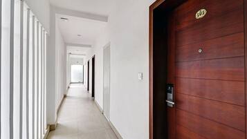 A corridor with a wooden door on the right, white walls, and a tiled floor.