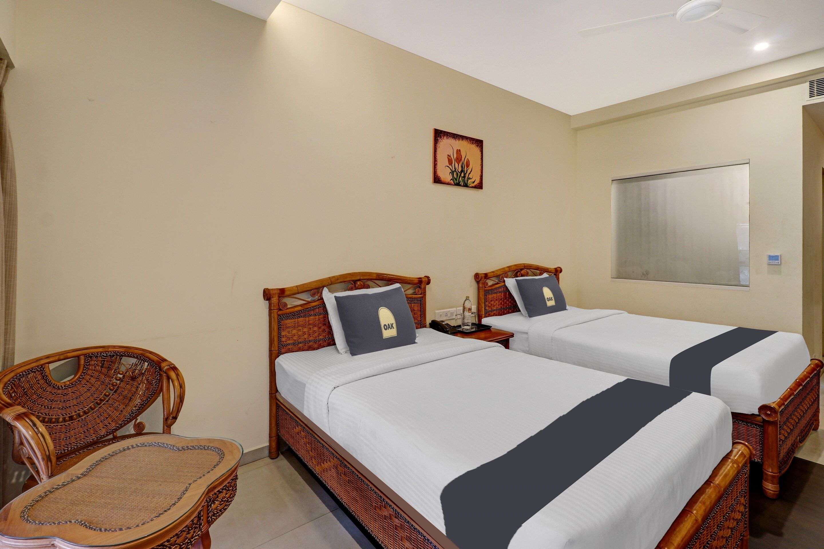 A hotel room with two beds, a chair, a small table, and a wall-mounted air conditioner.