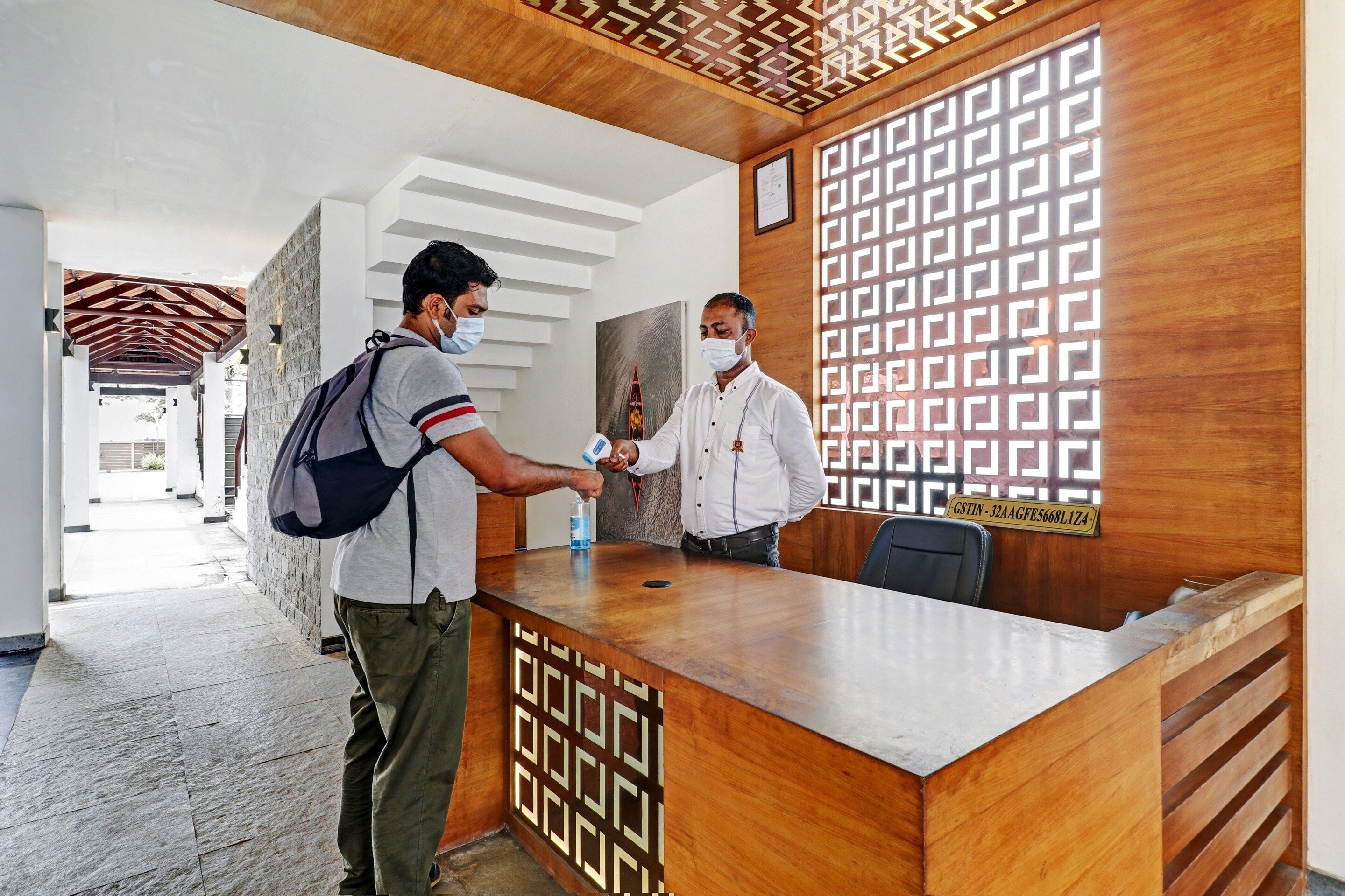 A reception desk with a patterned wooden design, a man handing over a document, and another man standing beside it.