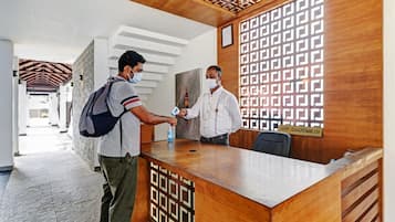 A reception desk with a patterned wooden design, a man handing over a document, and another man standing beside it.