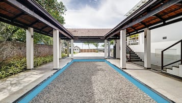 Un espacio exterior cubierto con piscina, columnas y una escalera que lleva a un nivel superior.