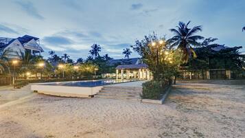 A resort with a pool, palm trees, and a building with a tiled roof.