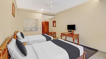 Habitación de hotel con dos camas, televisión, escritorio y ventilador de techo.