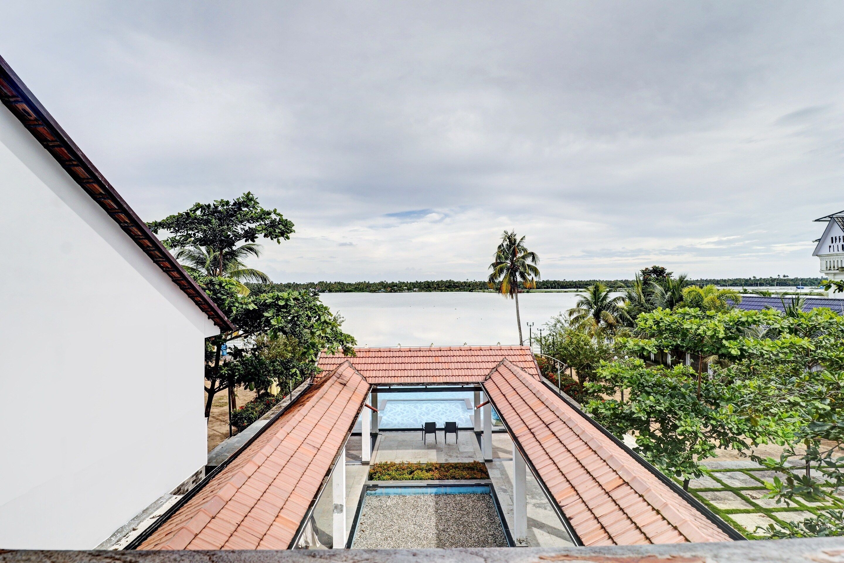 A rooftop terrace with a pool, surrounded by greenery and overlooking a body of water.