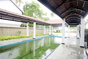 A covered swimming pool area with a tiled roof, white pillars, and a stone wall.