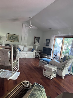 A living room with a white sofa, a wicker chair, a television, and a large window. - Enjoyable 2-bedroom house in Hilton Head Island (Hilton Head Island)