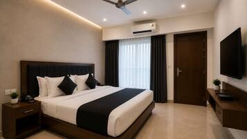 A modern hotel room with a large bed, a ceiling fan, an air conditioning unit, a TV, and a small bedside table with a plant.