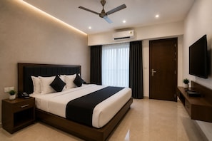 A modern hotel room with a large bed, a ceiling fan, an air conditioning unit, a TV, and a small bedside table with a plant.