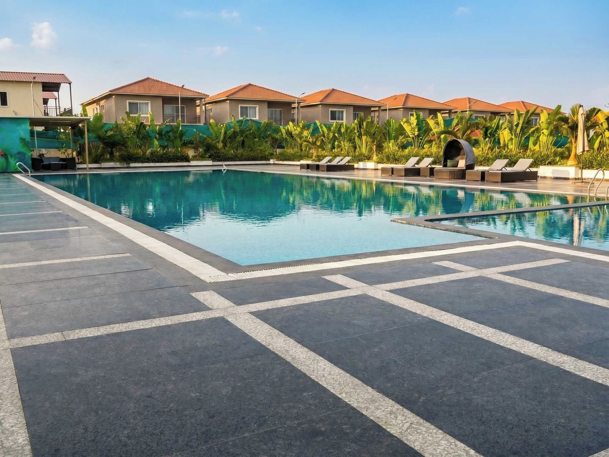 Una piscina con sillones de descanso y una terraza con baldosas.