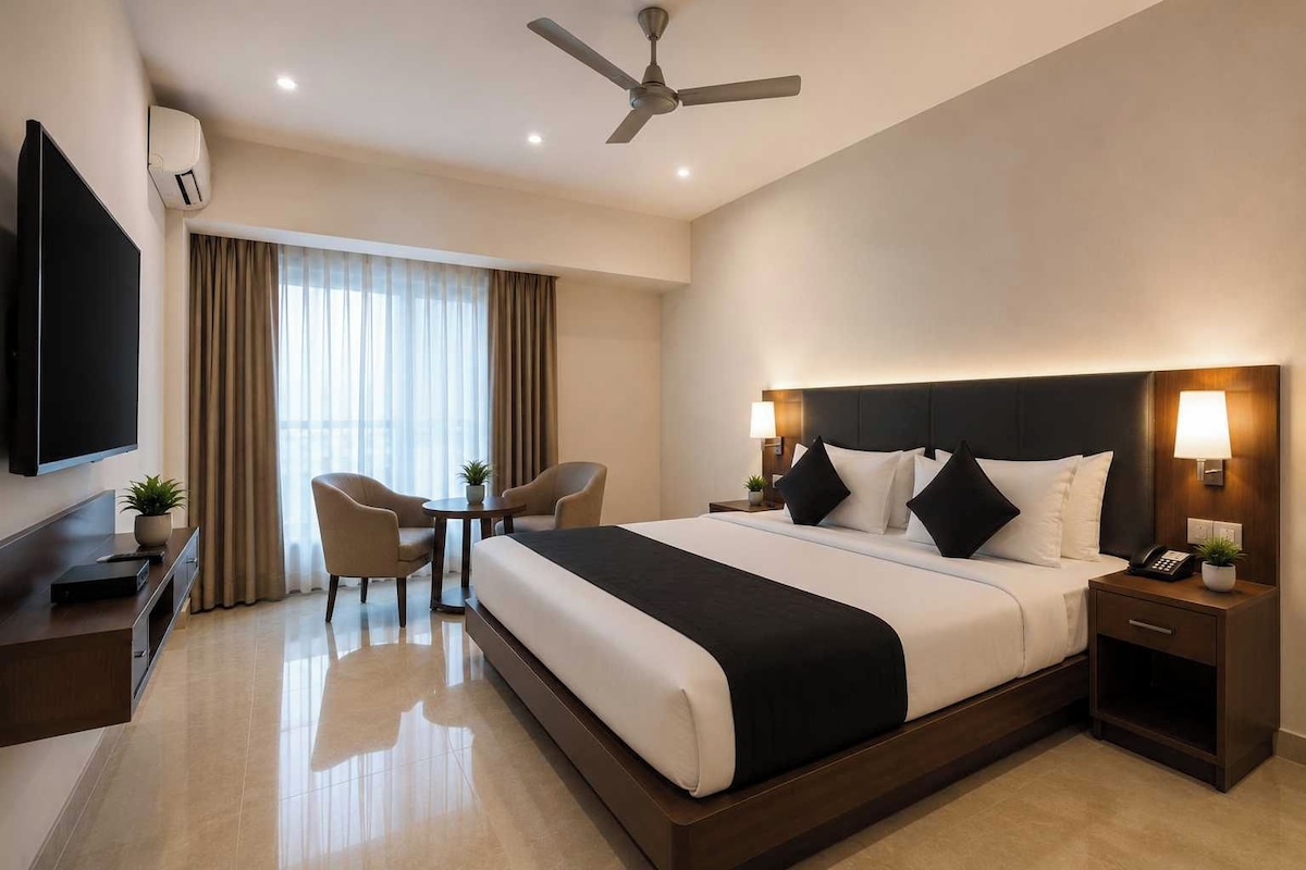 Une chambre d’hôtel avec un grand lit, un bureau, une chaise, une télévision et un ventilateur de plafond.