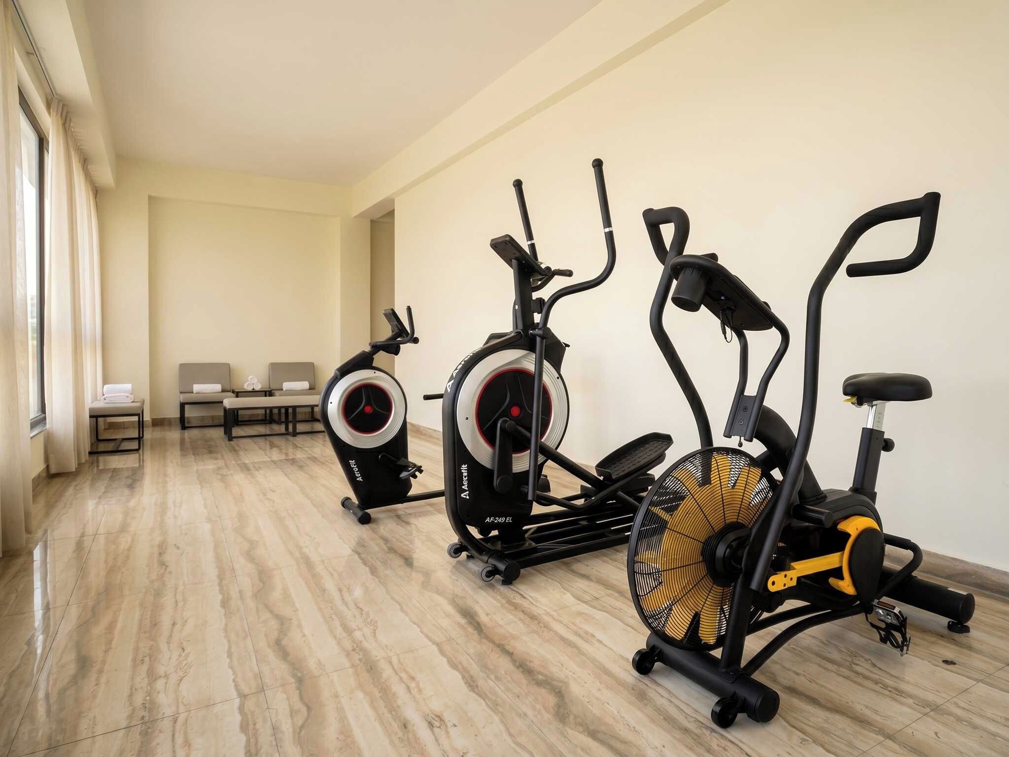 Quarto de hotel com área de ginástica, incluindo duas bicicletas ergométricas e um banco.