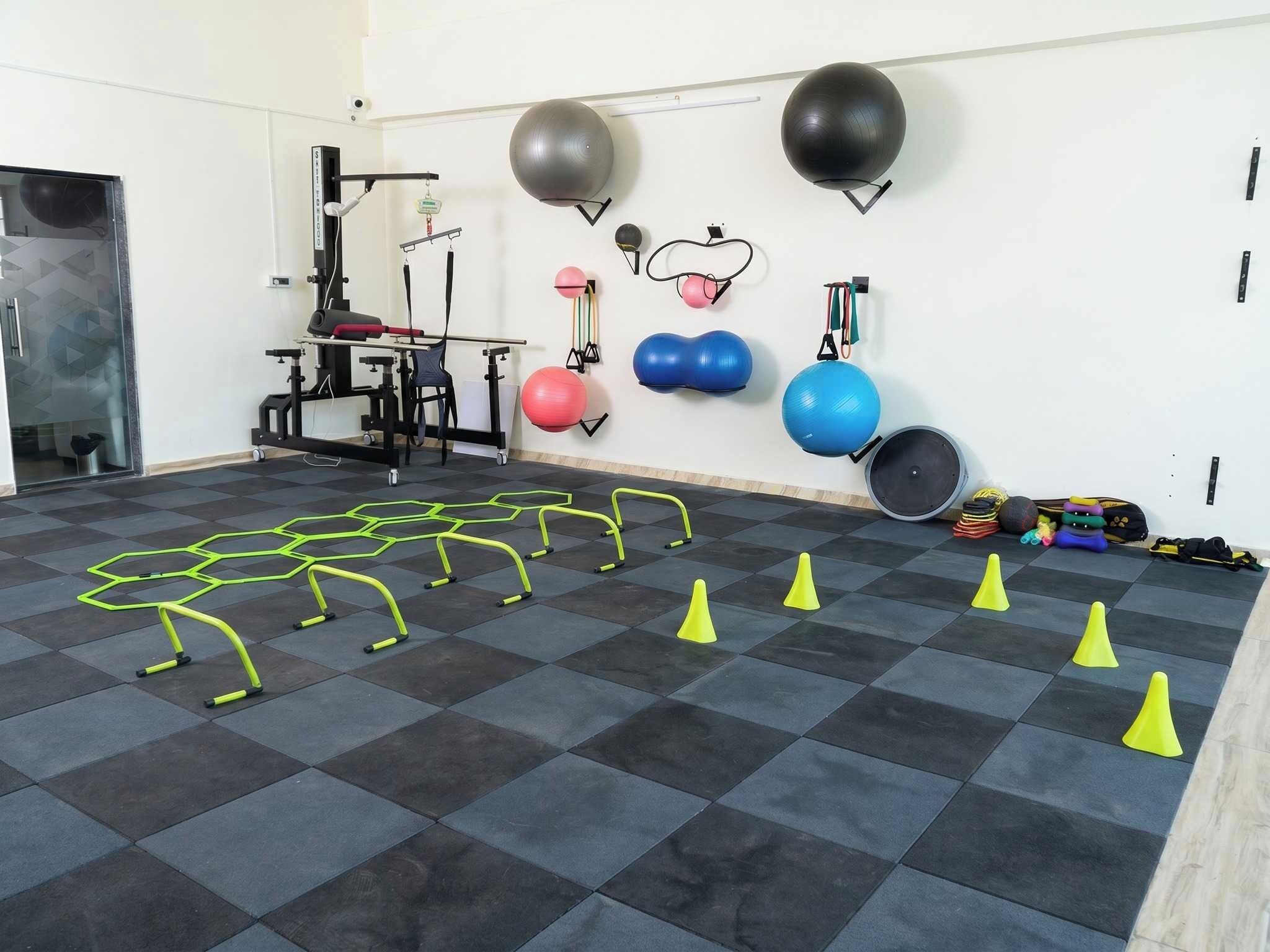 A gym with exercise equipment, a wall-mounted medicine ball rack, and a floor with agility cones.
