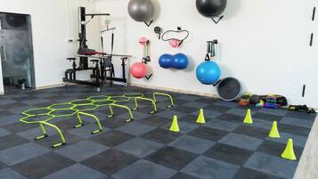 A gym with exercise equipment, a wall-mounted medicine ball rack, and a floor with agility cones.