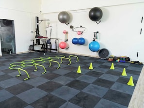 Une salle de sport équipée de matériel d’exercice, d’un support mural pour balles lestées et d’un sol agrémenté de cônes pour les exercices d’agilité.