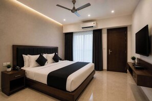 A modern hotel room with a large bed, a ceiling fan, an air conditioning unit, a television, and a door.
