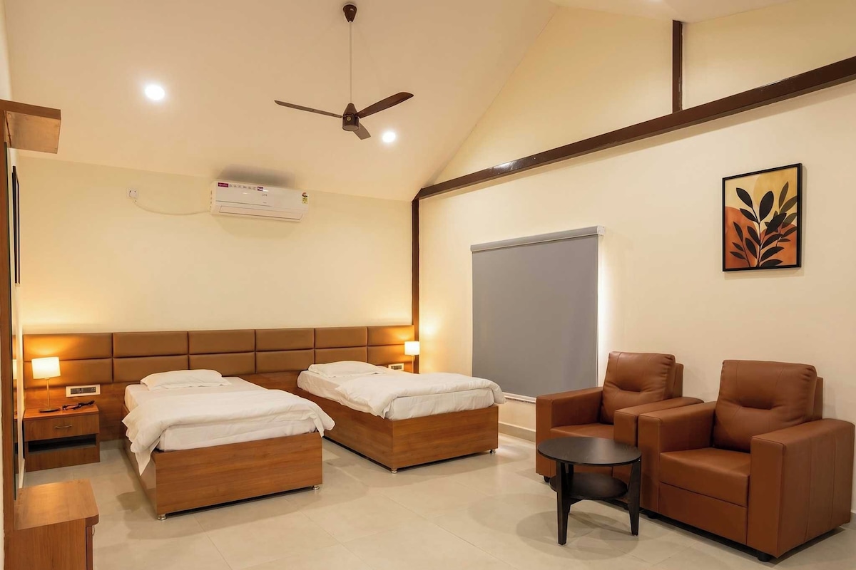 Une chambre d’hôtel avec deux lits, un canapé, une petite table, un ventilateur de plafond et un appareil de climatisation.