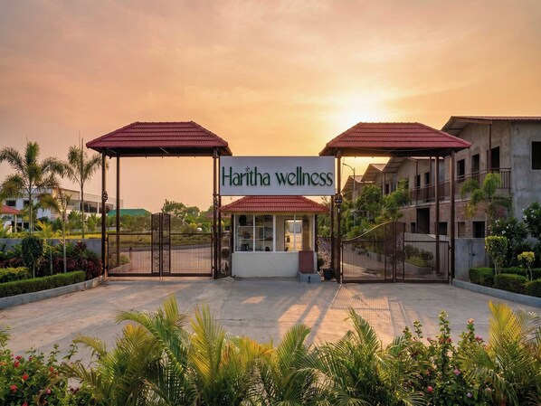 A wellness center named 'Haritha wellness' with a gated entrance, covered walkways, and a landscaped garden.