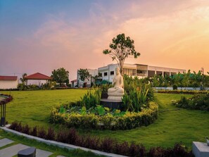 A serene garden with a Buddha statue, lush greenery, and a modern building in the background. - Palette Haritha Wellness Resort CheckIn (Momanpet)