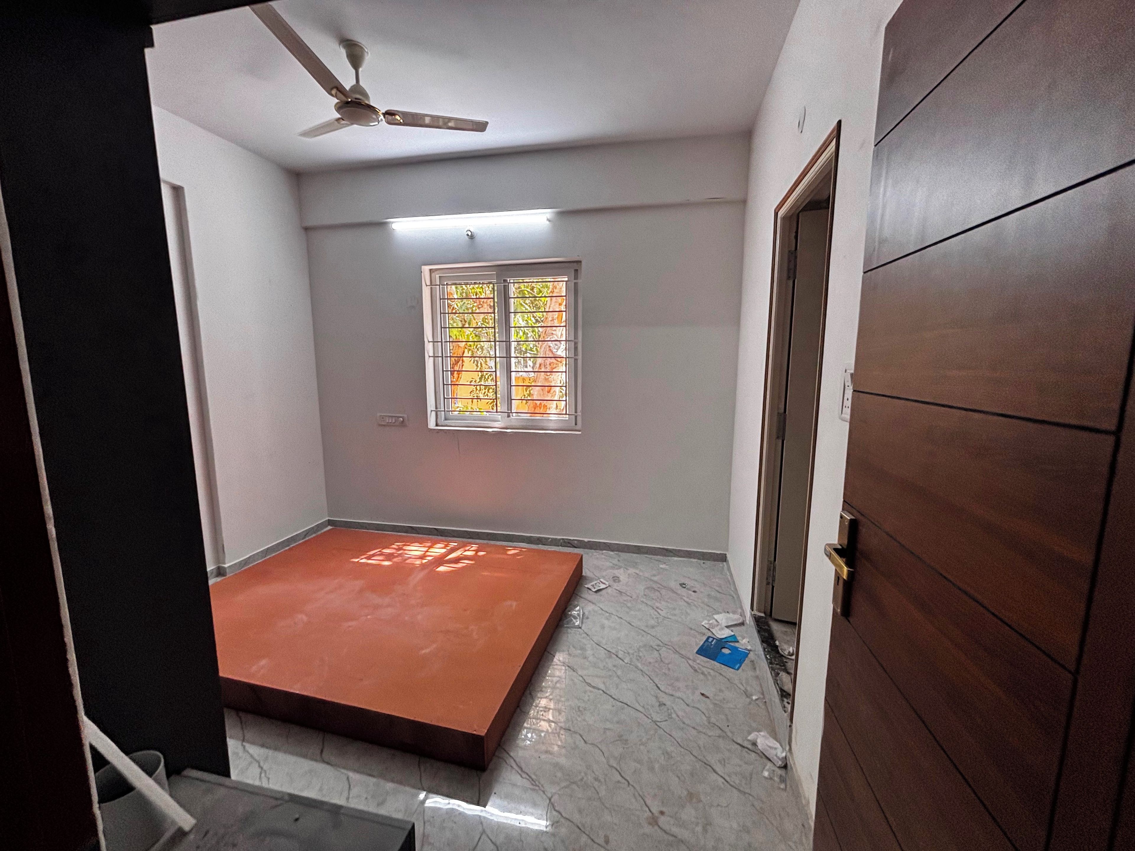 Una habitación con ventilador de techo, ventana con rejas y una puerta.