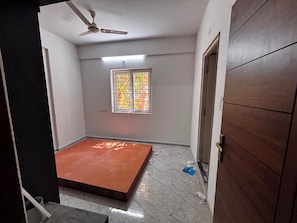 A room with a ceiling fan, a window with bars, and a door.