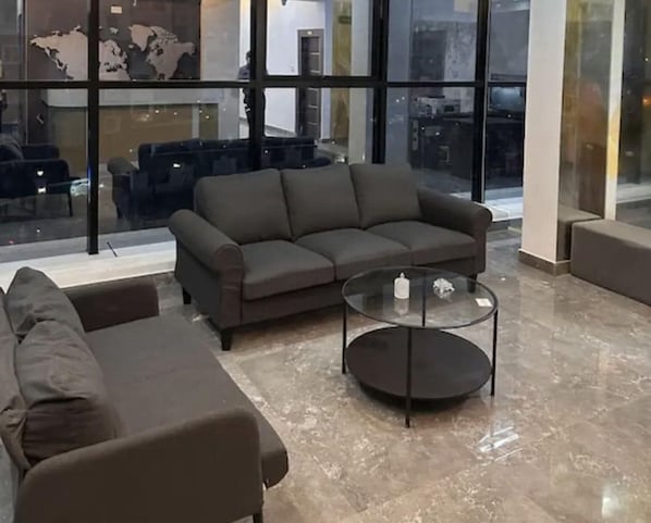 A modern living room with a sectional sofa, a glass coffee table, and a large window offering a view of the cityscape.